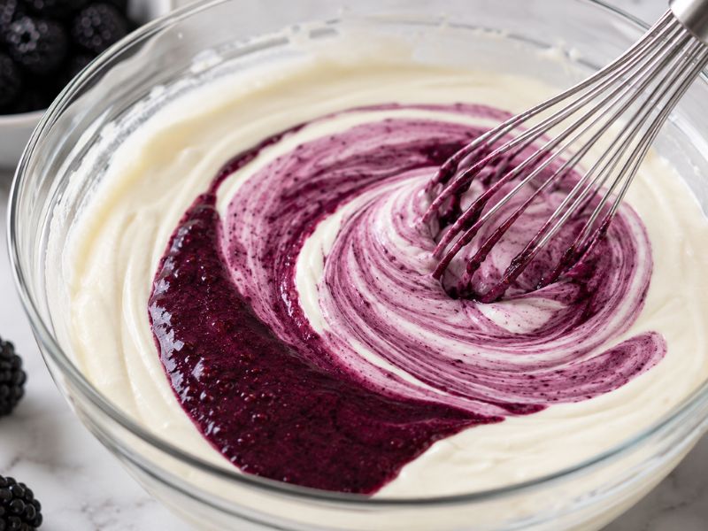 Blackberry puree being mixed into a creamy ice cream base