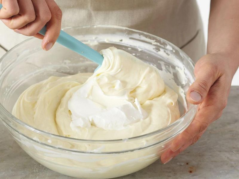 Folding whipped cream into the cream cheese base for cheesecake ice cream