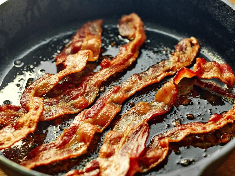 Crispy bacon cooking in a skillet for homemade maple bacon ice cream