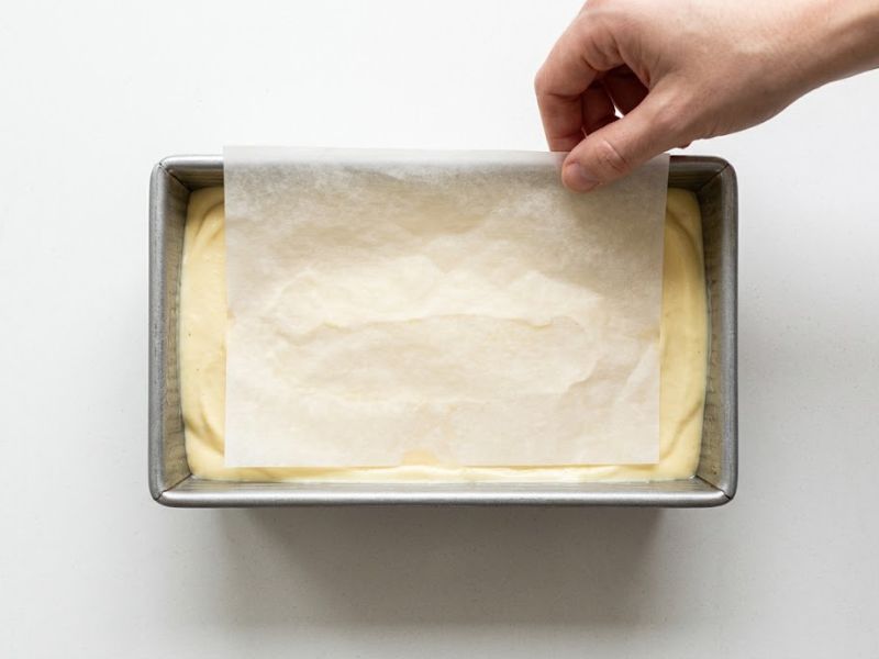 Pineapple ice cream mixture in a loaf pan topped with parchment paper before freezing